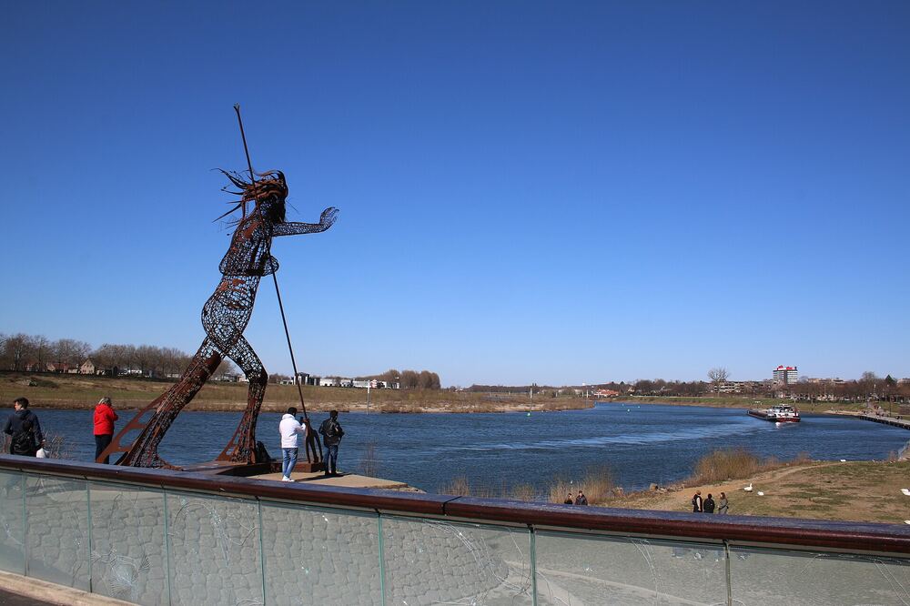 Wandelaars langs de Maas bij Venlo, met het beeld de Vreedzame Krijger op de kade